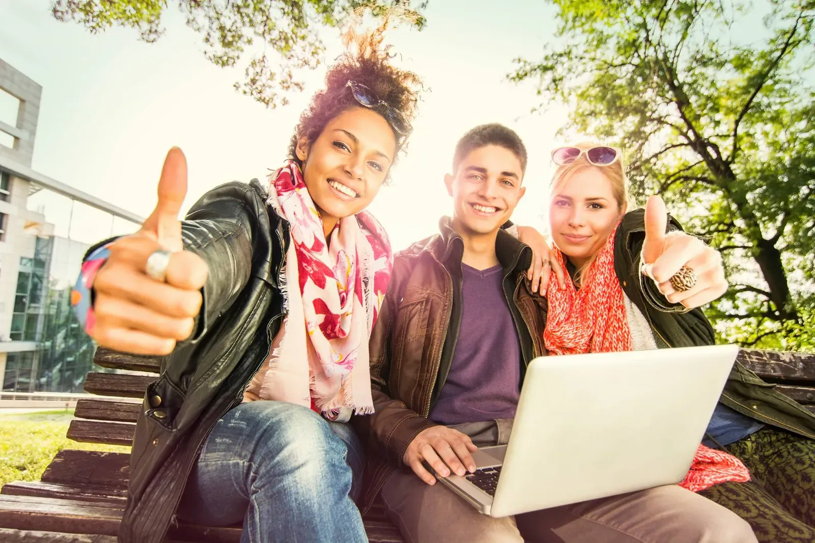 Three young people outdoors with a laptop giving a thumbs up