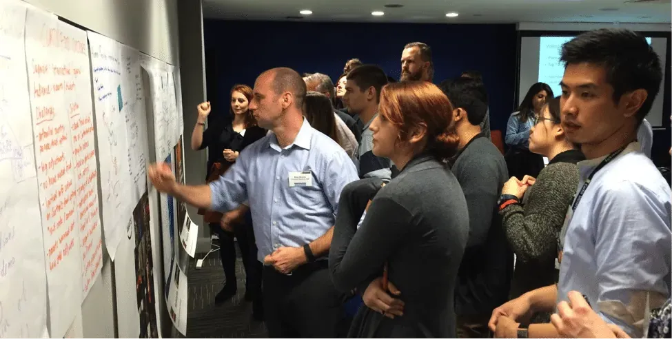 Hackathon participants reviewing handwritten idea notes pinned to a workshop wall