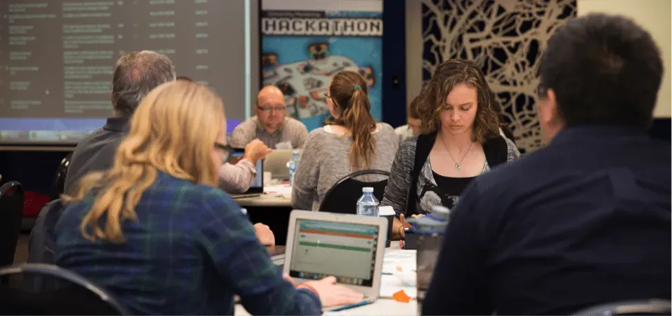 Hackathon participants working on laptops at tables beneath a Hackathon banner