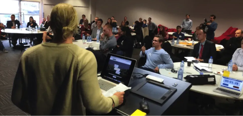Hackathon participant pitching to a seated audience with a countdown timer running