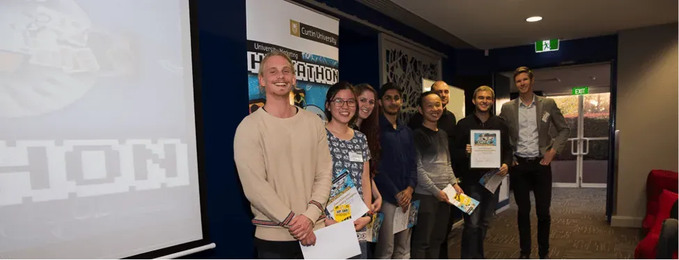 Winning hackathon team holding certificates in front of a Curtin University Hackathon banner